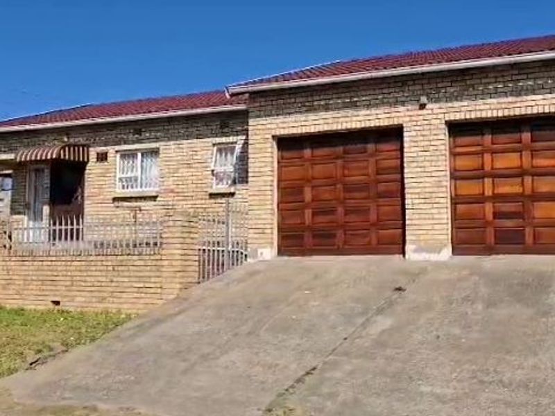 Front exterior view of a face brick house featuring a double garage, concrete driveway, and perimeter wall with security fencing.