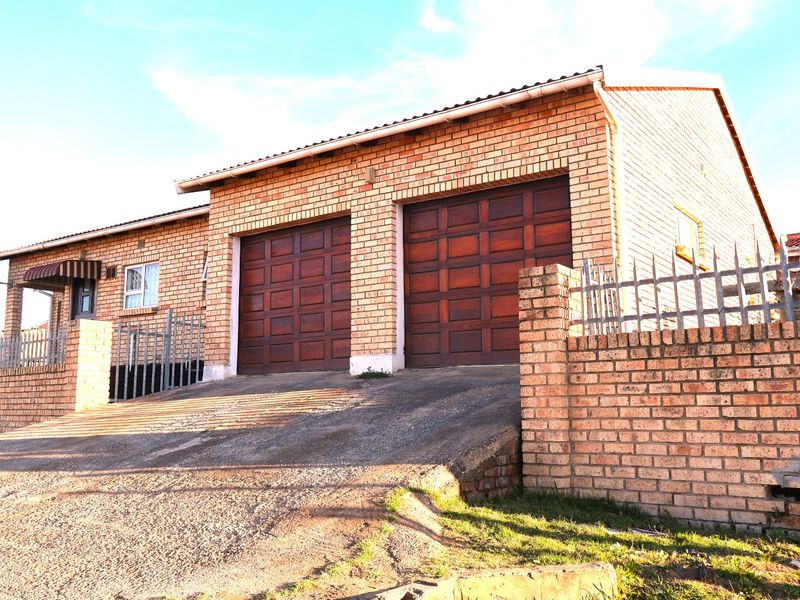 Front view of a brick house featuring a double garage, concrete driveway, and perimeter wall with security fencing.