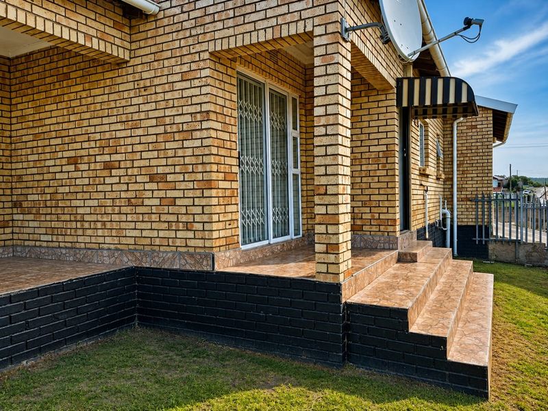 A covered brick patio featuring tiled flooring and steps, providing an outdoor entrance area with a security gate and awning.