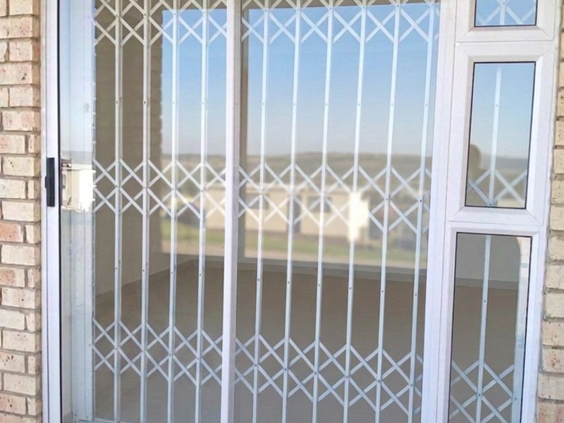 A covered patio area featuring a sliding glass door with integrated security gate, brick exterior walls, and tiled flooring.