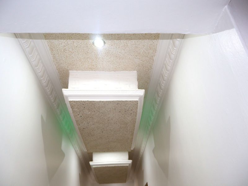 A narrow hallway featuring decorative ceiling cornices and recessed ceiling panels with integrated downlighting.