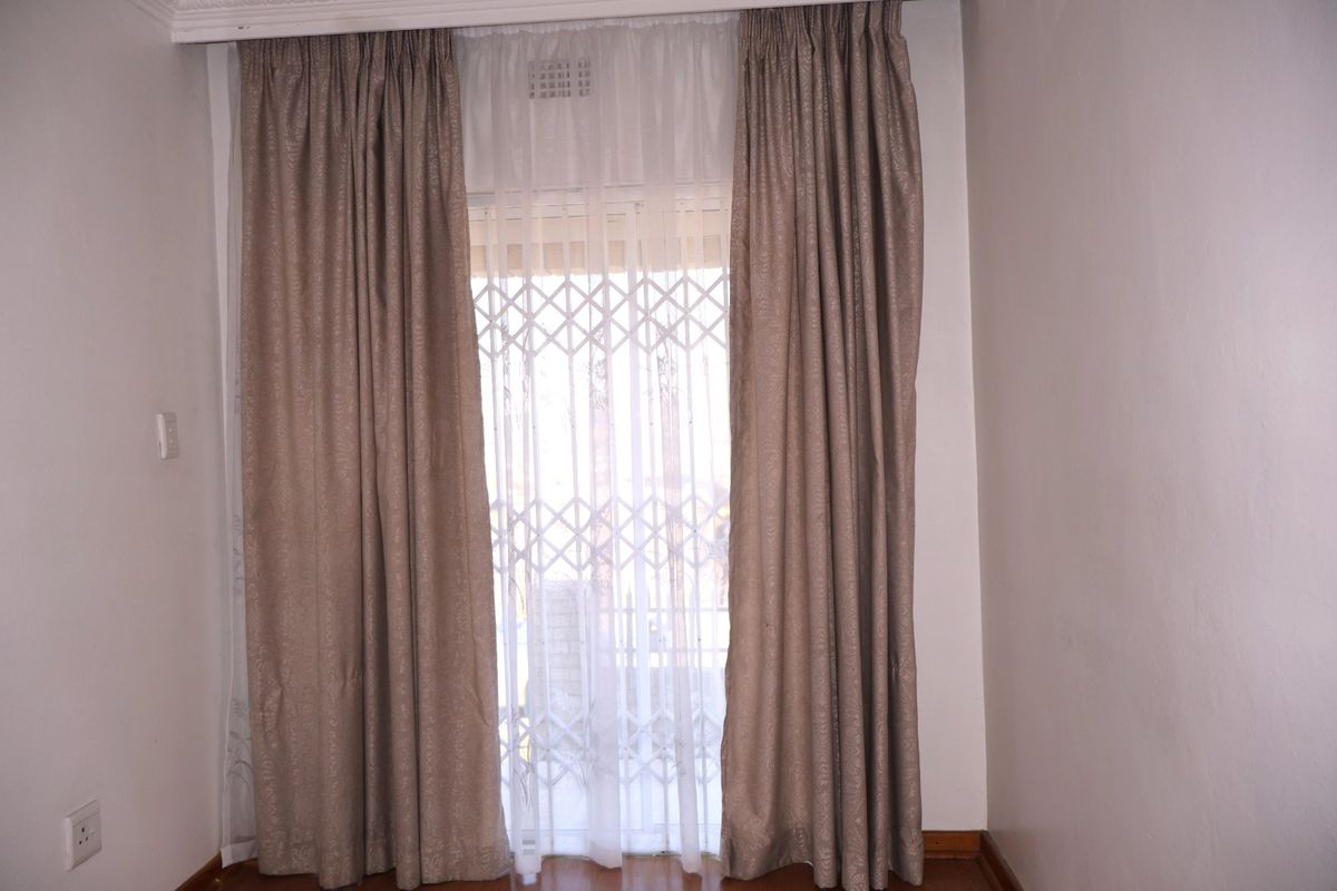 A bright, empty bedroom featuring laminate flooring, neutral walls, and a secure sliding door with a fitted security gate.