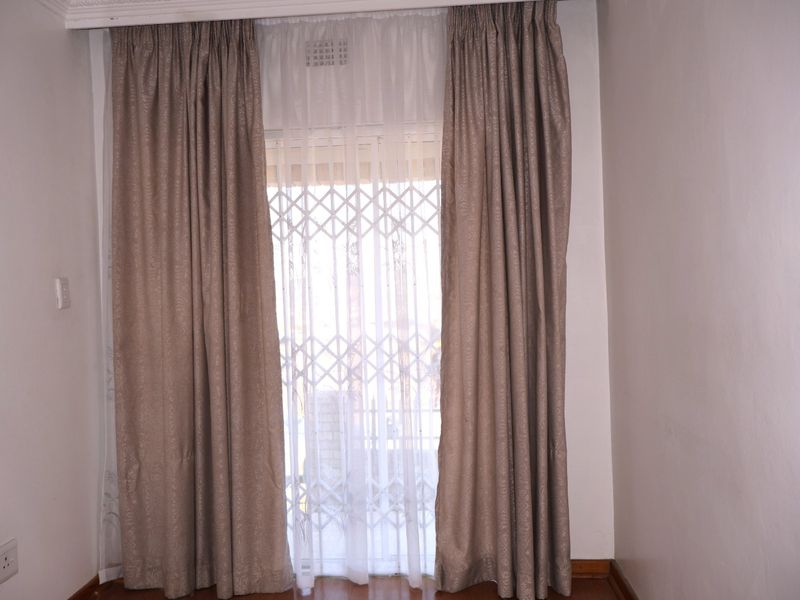 A bright, empty bedroom featuring laminate flooring, neutral walls, and a secure sliding door with a fitted security gate.