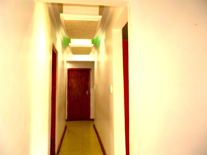 A narrow interior hallway featuring tiled flooring, timber doors, and recessed ceiling panels with integrated lighting.