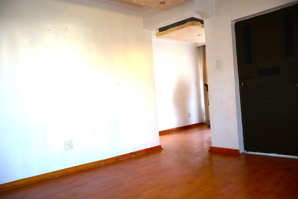 An empty living area featuring laminate flooring, timber skirting boards, and a unique recessed ceiling detail, offering a blank canvas for interior design.