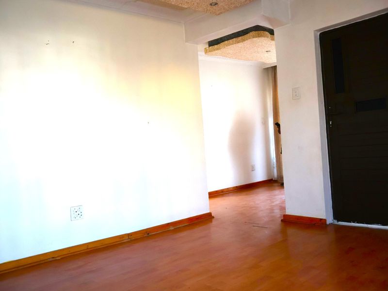 An empty living area featuring laminate flooring, timber skirting boards, and a unique recessed ceiling detail, offering a blank canvas for interior design.