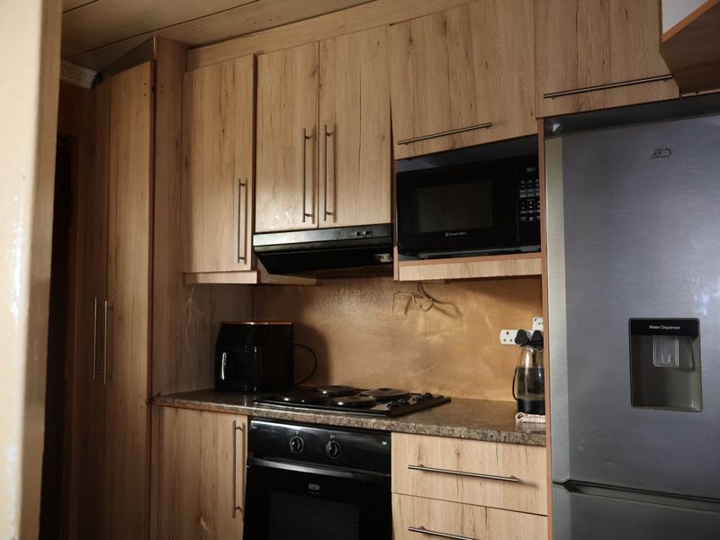 A compact kitchen featuring wood-look cabinetry, integrated appliances including an oven and hob, and a functional layout with ample storage space.