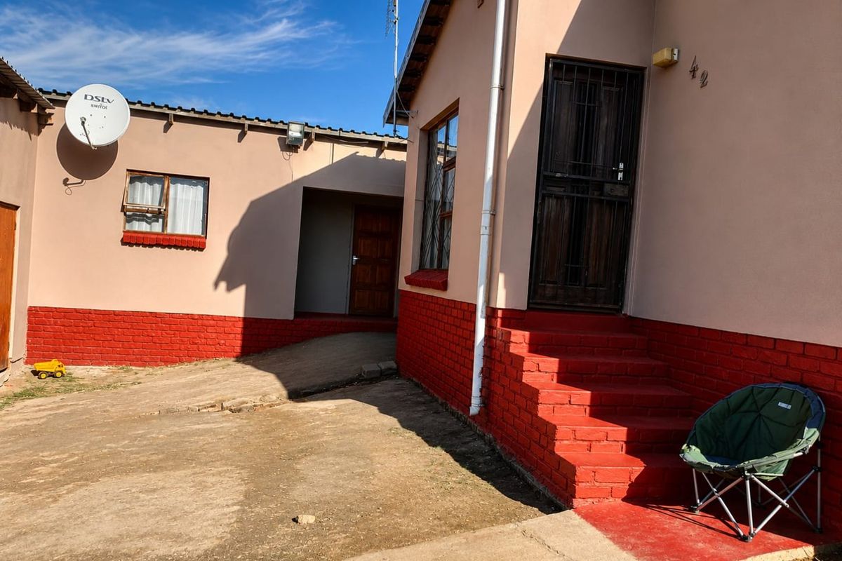 Rear exterior view of the property featuring a concrete courtyard, painted brick base, and secure entrance doors.