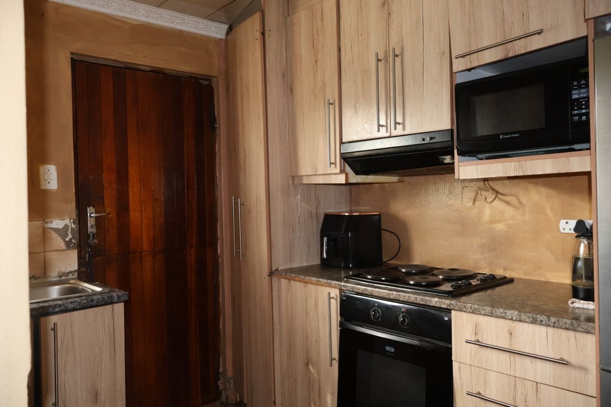 A compact kitchen featuring wood-look cabinetry, built-in oven and hob, and a stainless steel sink, requiring some cosmetic wall repairs.