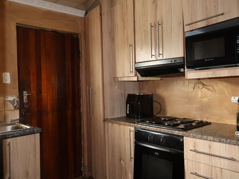 A compact kitchen featuring wood-look cabinetry, built-in oven and hob, and a stainless steel sink, requiring some cosmetic wall repairs.