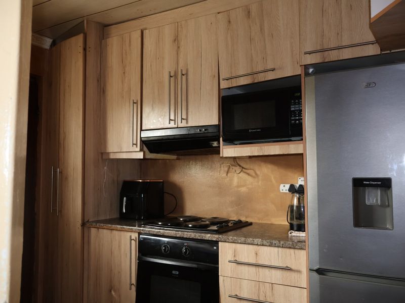 A functional kitchen featuring wood-look cabinetry, integrated appliances including an oven, hob, and microwave, with stone-effect countertops.