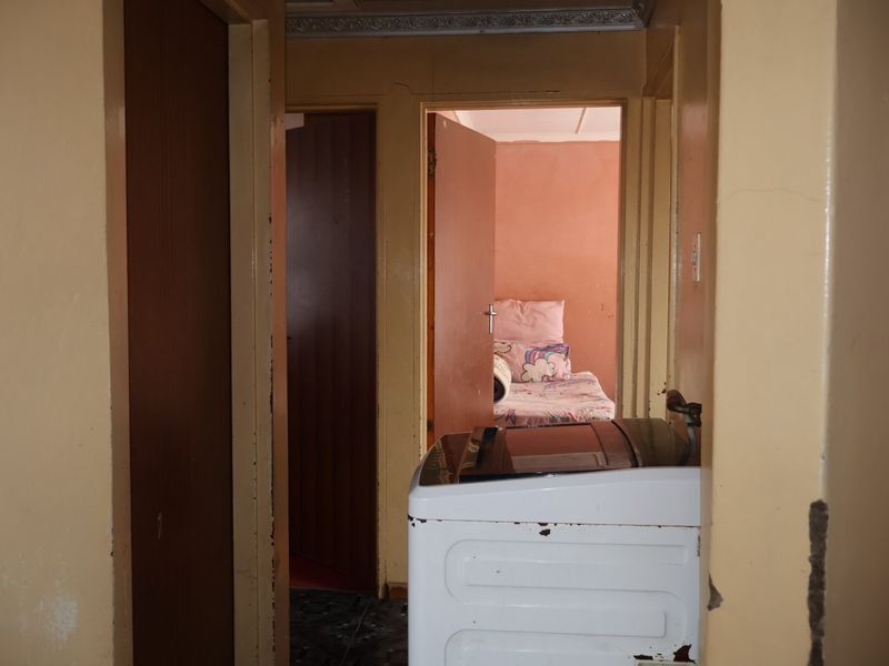 A narrow interior hallway showing signs of wear, including peeling paint and damaged wall surfaces, leading into adjacent rooms.
