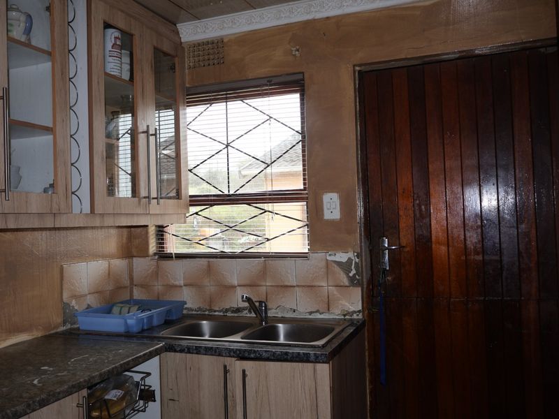 Kitchen area featuring laminate cabinetry, a double stainless steel sink, and tiled splashback, requiring cosmetic updates to the wall finishes and tiling.