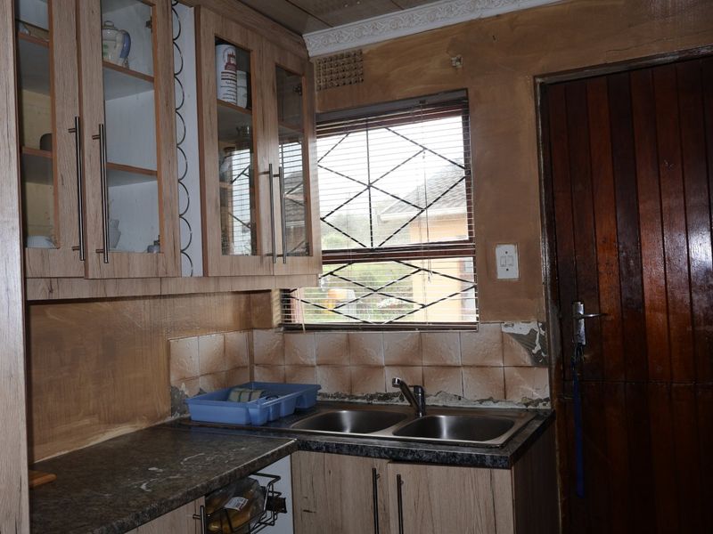 A kitchen area featuring laminate cabinetry, a double bowl sink, and tiled splashbacks, currently requiring wall repairs and cosmetic updates.