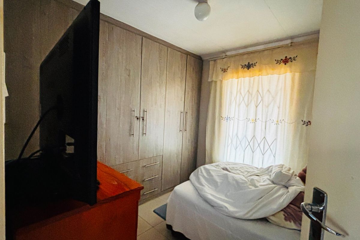A functional bedroom featuring built-in wooden cupboards and a security gate on the window, providing essential storage and security.