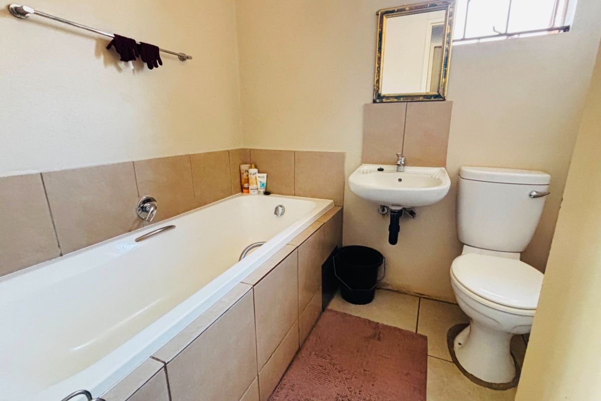 A functional bathroom featuring a built-in bathtub, wall-mounted basin, and toilet with neutral wall and floor tiling.