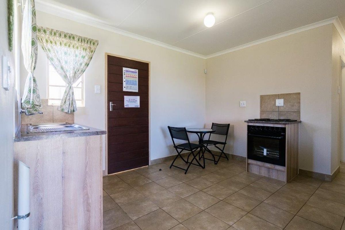 A functional kitchen area featuring tiled flooring, built-in cabinetry with laminate countertops, a stainless steel sink, and a freestanding oven with a tiled splashback.