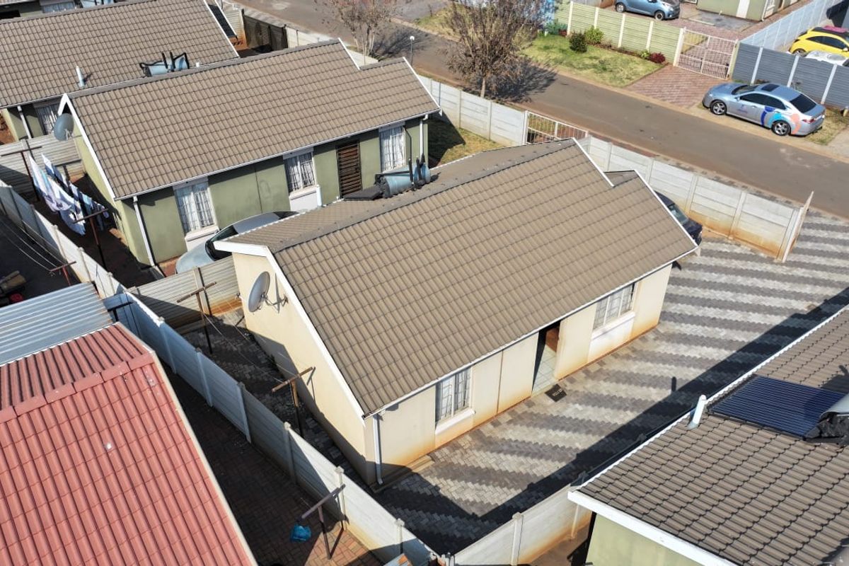 Aerial view of a residential property featuring a tiled roof, paved driveway, and perimeter precast concrete walling in a suburban setting.