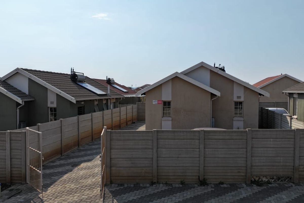 Rear view of a residential property featuring a paved driveway, precast concrete boundary walls, and solar water heating systems on the tiled roof.