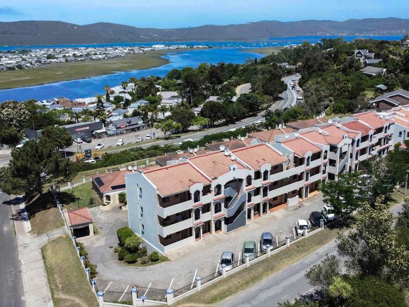 Aerial view of a multi-story apartment complex featuring terracotta tiled roofs, external stairwells, and a paved parking area with perimeter fencing.