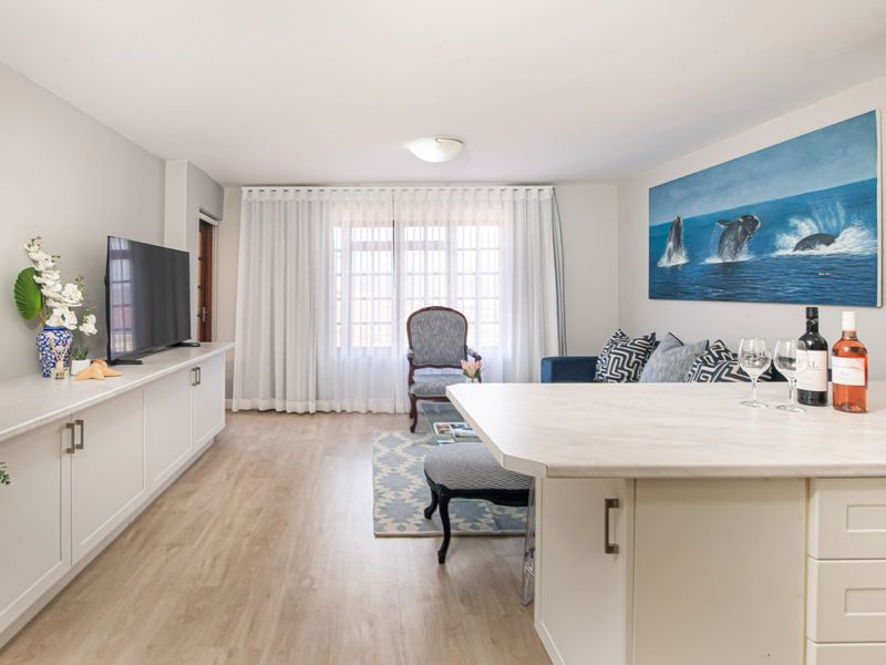 A bright open-plan living and kitchen area featuring modern built-in cabinetry, light laminate flooring, and a functional kitchen island.