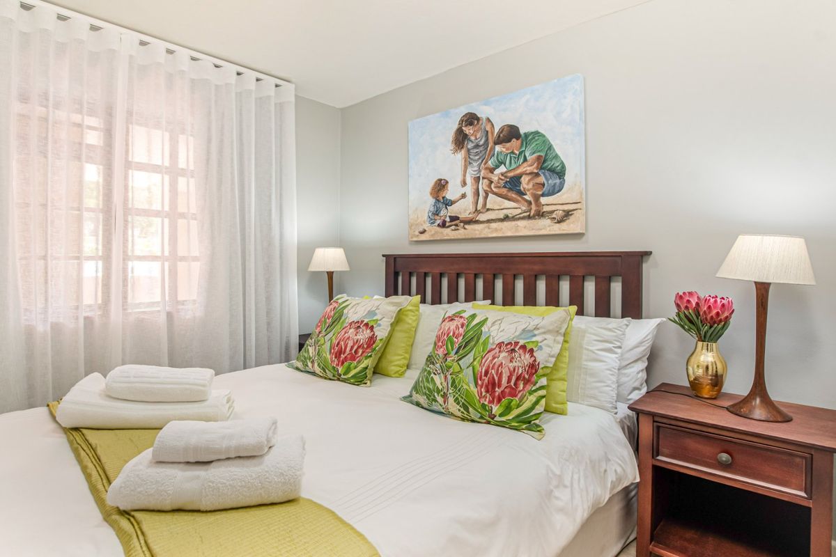 A well-maintained bedroom featuring neutral wall tones, a window with sheer curtains, and a classic wooden headboard.