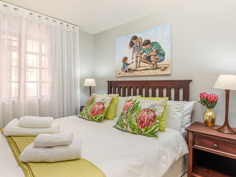 A well-maintained bedroom featuring neutral wall tones, a window with sheer curtains, and a classic wooden headboard.