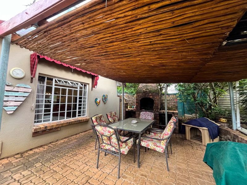 Covered outdoor patio area featuring a brick-built braai, paved flooring, and a rustic thatched pergola, ideal for outdoor entertaining.