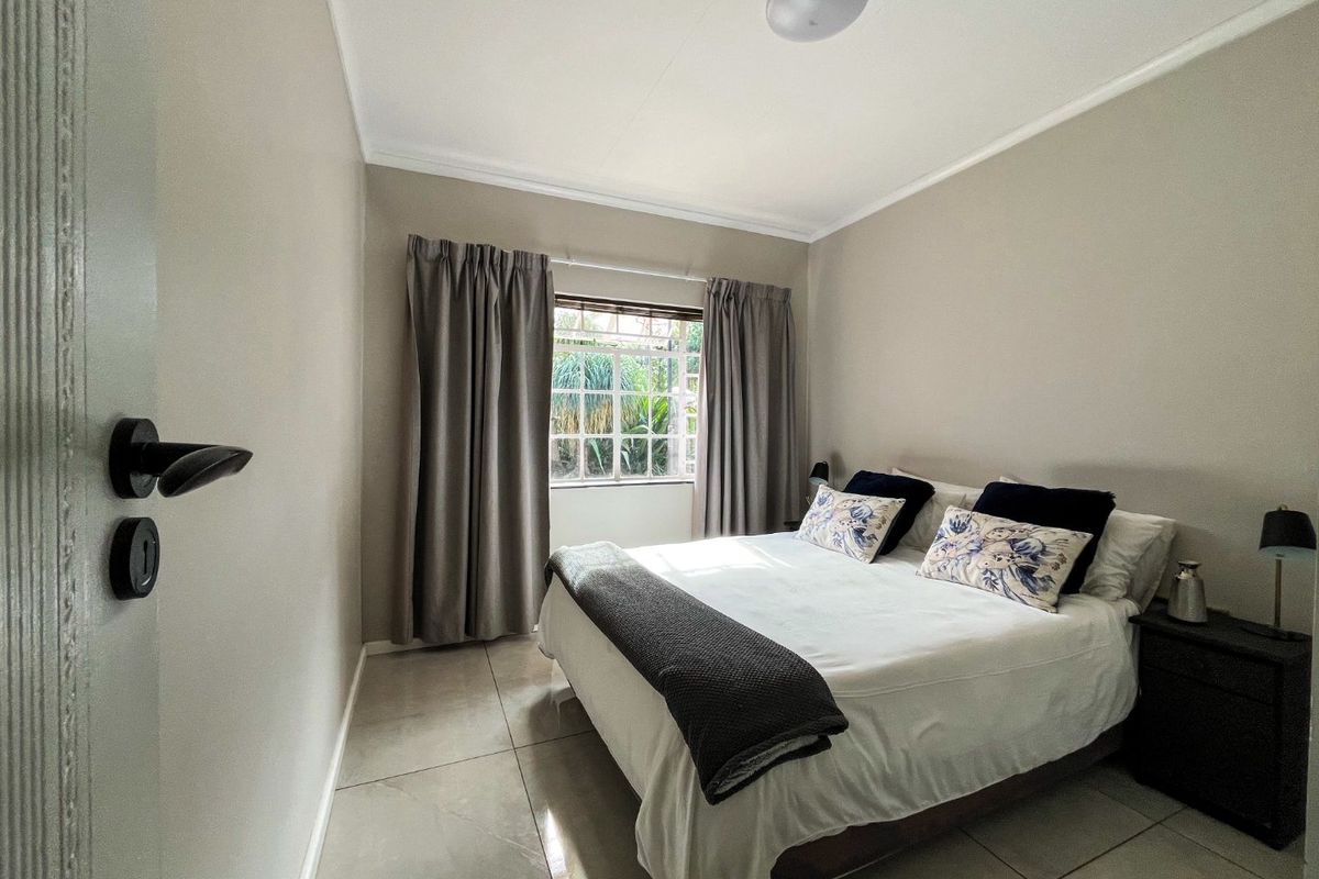 A well-maintained bedroom featuring neutral wall tones, large format floor tiles, and a window with security bars providing natural light.