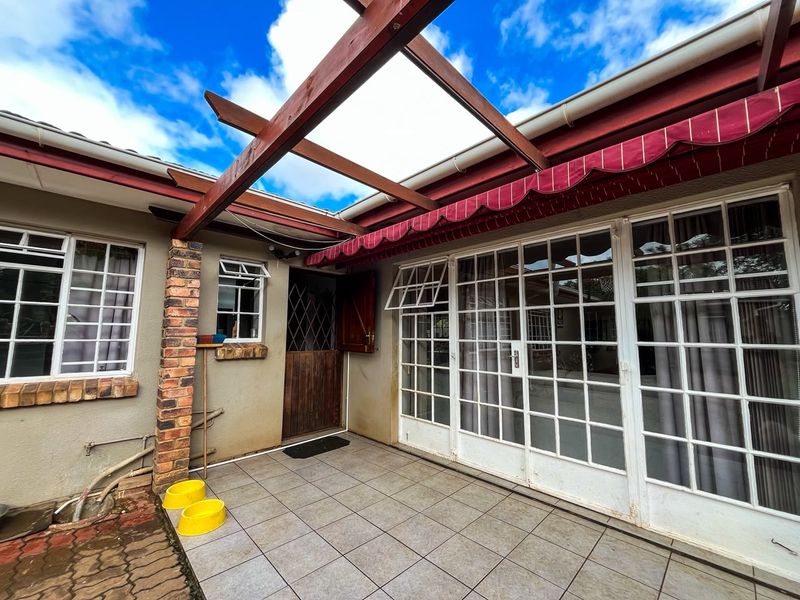 Covered patio area featuring a timber pergola, retractable awning, and tiled flooring, providing direct access to the home through classic french doors.