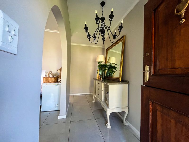 A welcoming entrance hall featuring tiled flooring, a decorative archway, and a classic wrought iron chandelier, leading into the main living area.