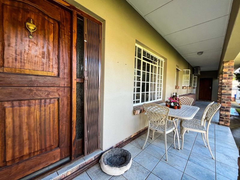 A covered patio area featuring tiled flooring, a solid timber front door with security gate, and security bars on the windows.