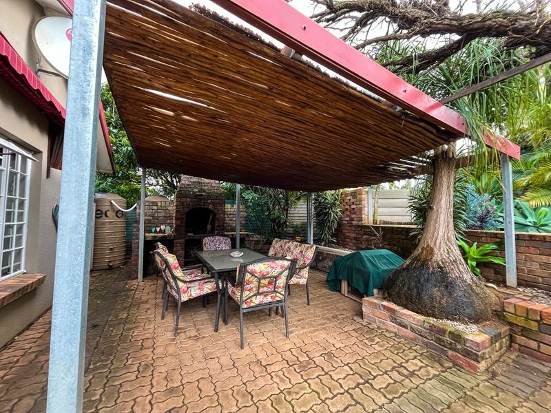 Outdoor patio area featuring a brick built-in braai, paved flooring, and a thatched roof pergola, providing a functional space for outdoor entertaining.