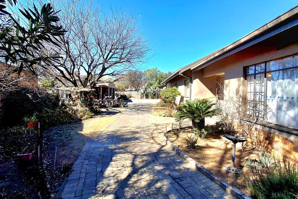 A view of the rear exterior of the house featuring a paved driveway, brick facade, and established garden area.