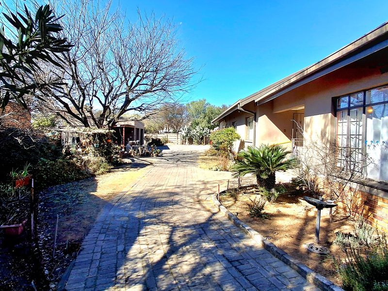 A view of the rear exterior of the house featuring a paved driveway, brick facade, and established garden area.