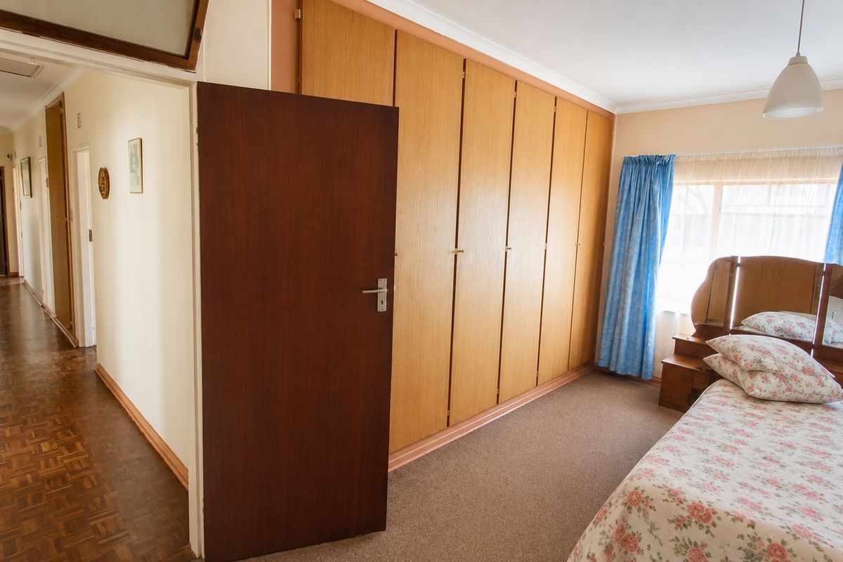 A bedroom featuring built-in wooden cupboards, carpeted flooring, and access to a parquet-floored hallway.