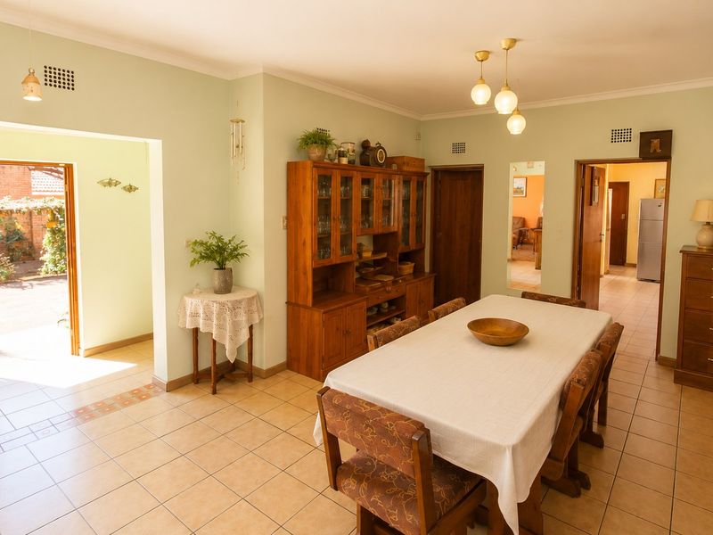 A spacious dining room featuring ceramic floor tiles, coved ceilings, and direct access to an outdoor area through a timber-framed door.
