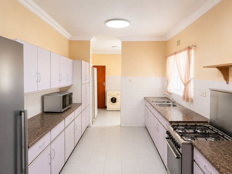 A functional kitchen featuring laminate countertops, built-in cabinetry, a gas hob, and a double sink, with an adjacent laundry area visible.