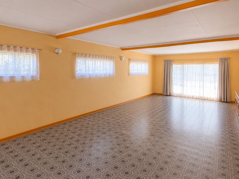 Spacious, empty living area featuring tiled flooring, exposed ceiling beams, and built-in cabinetry, offering a blank canvas for renovation.