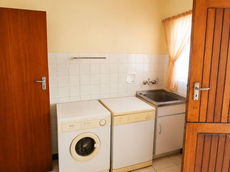 A functional laundry room featuring a stainless steel sink, tiled splashback, and space for laundry appliances, finished with timber doors.