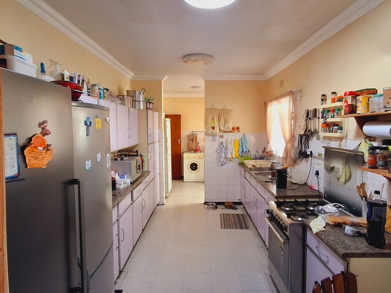 Functional galley-style kitchen featuring built-in cabinetry, gas hob, oven, and tiled splashbacks, with an adjacent laundry area visible in the background.