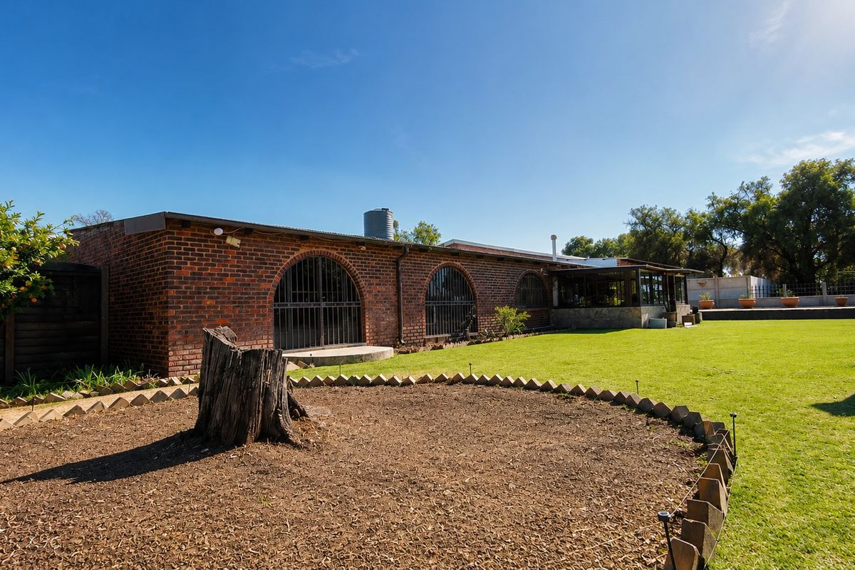 Rear view of a farm-style property featuring exposed brick walls, arched windows with security bars, and a well-maintained lawn and garden area.