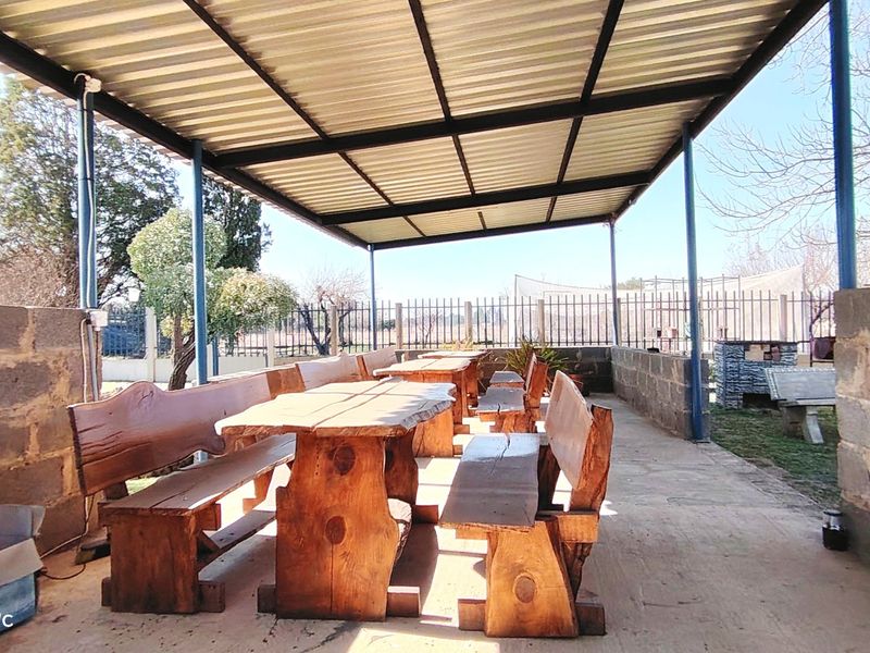 Covered outdoor patio area featuring a corrugated metal roof, steel supports, concrete flooring, and a built-in brick braai, ideal for farm-style entertaining.
