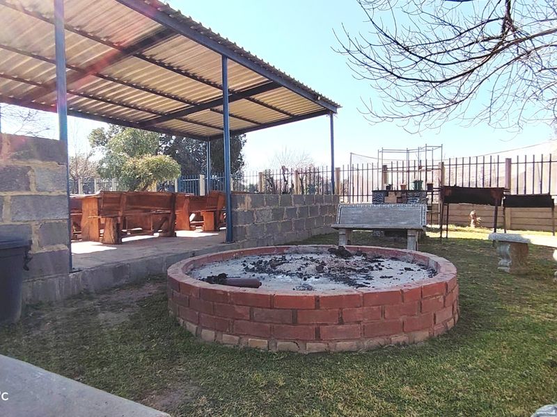 Outdoor entertainment area featuring a covered patio with a brick fire pit and perimeter fencing, suitable for farm-style gatherings.