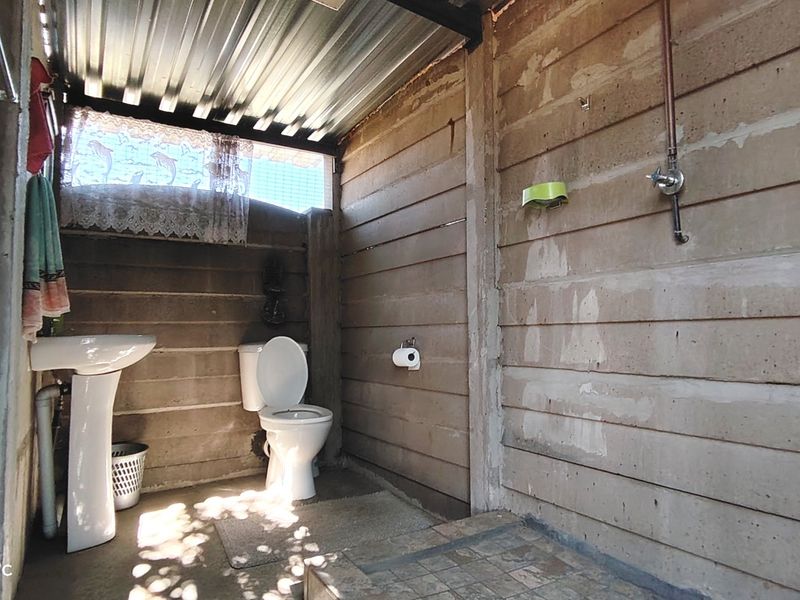 A basic bathroom featuring a pedestal basin and toilet with exposed concrete wall panels and a corrugated metal roof structure.