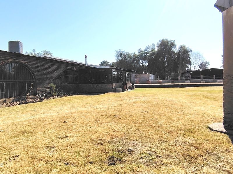 Rear view of the farm property featuring an exposed brick facade with arched windows and a covered patio area overlooking the lawn.