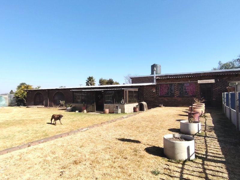 Rear view of a brick farmhouse featuring an enclosed patio, water tank, and expansive garden area with perimeter fencing.