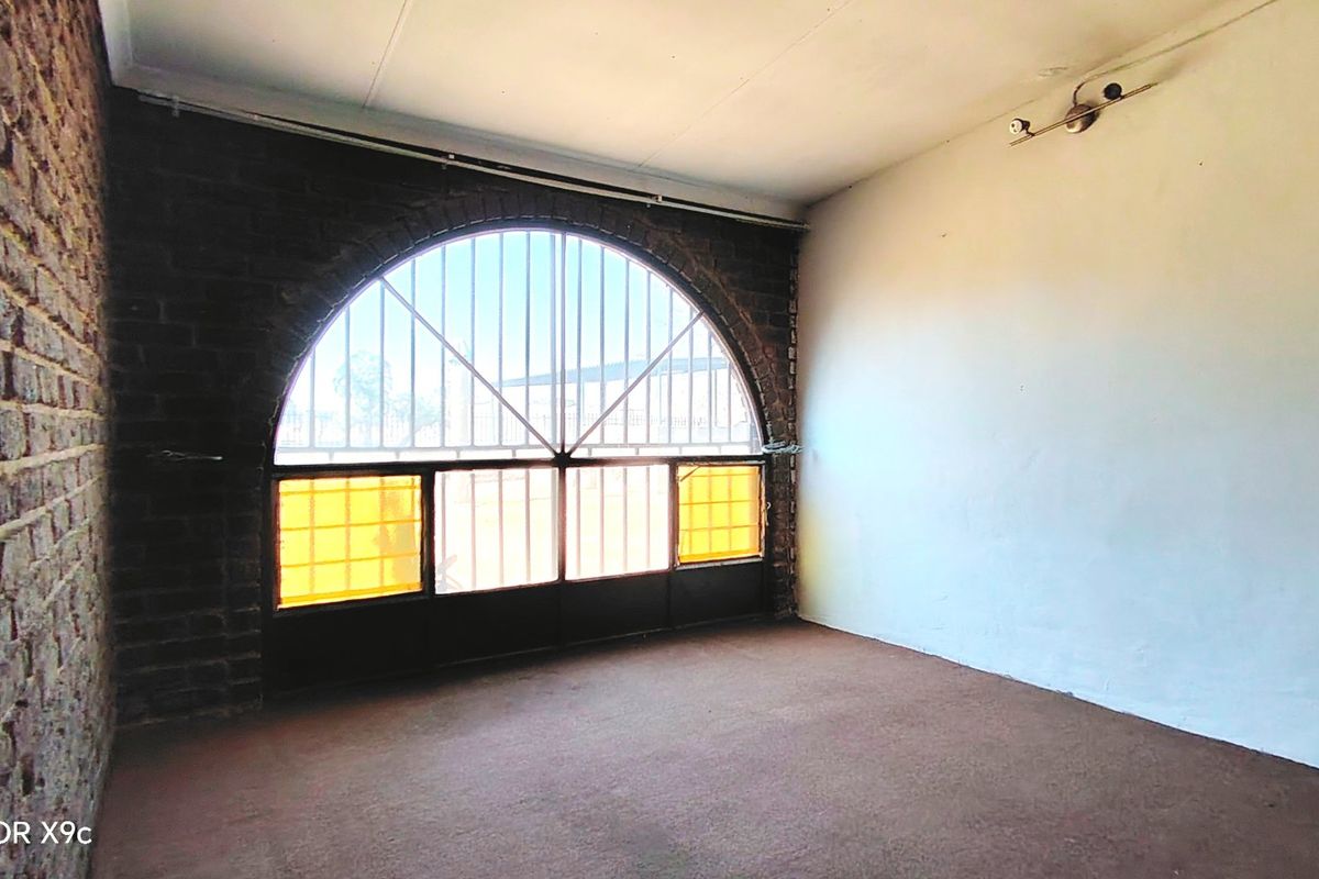 An empty living area featuring an exposed brick wall and a large arched window with security bars.
