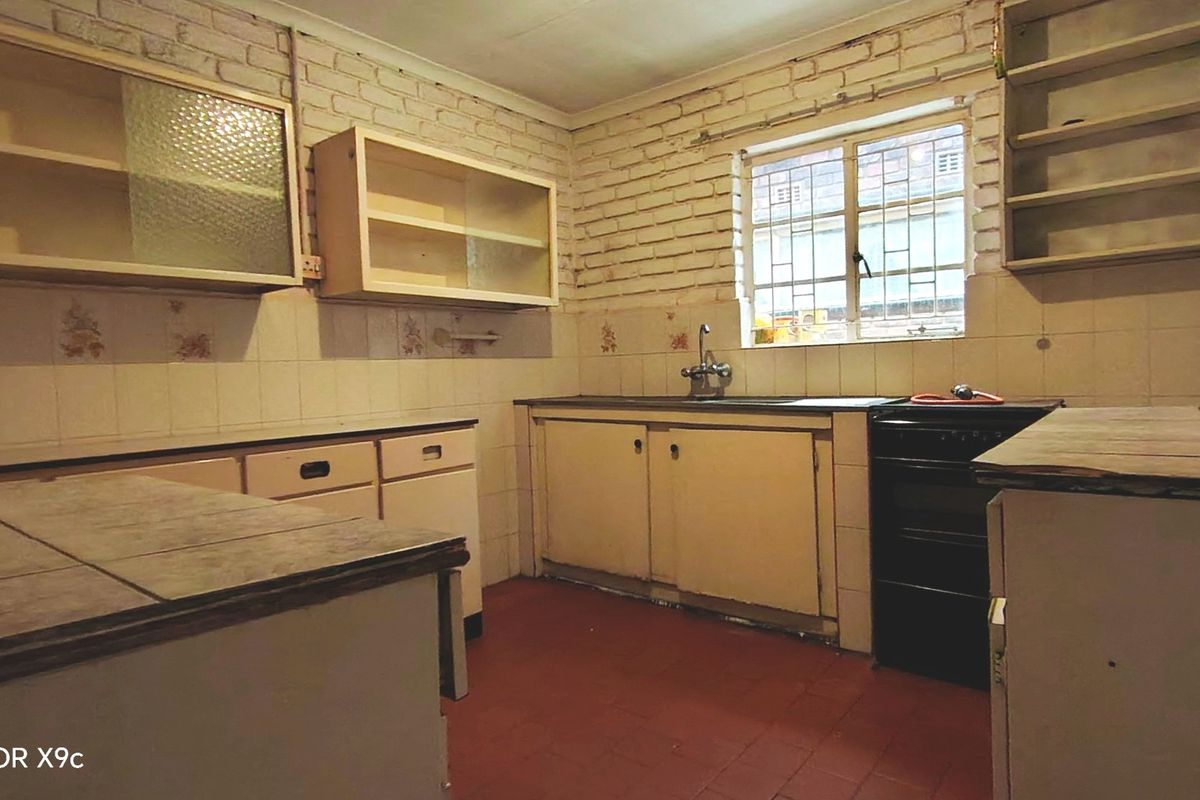 A dated kitchen featuring exposed brick walls, tiled countertops, and original cabinetry, offering significant potential for a modern renovation.