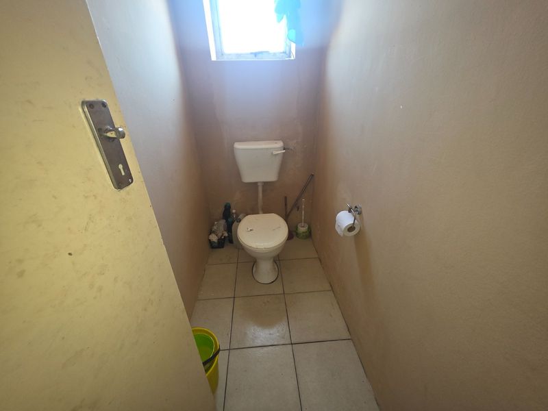 A small, functional guest toilet featuring tiled flooring and a window, currently requiring cosmetic updates and wall repairs.